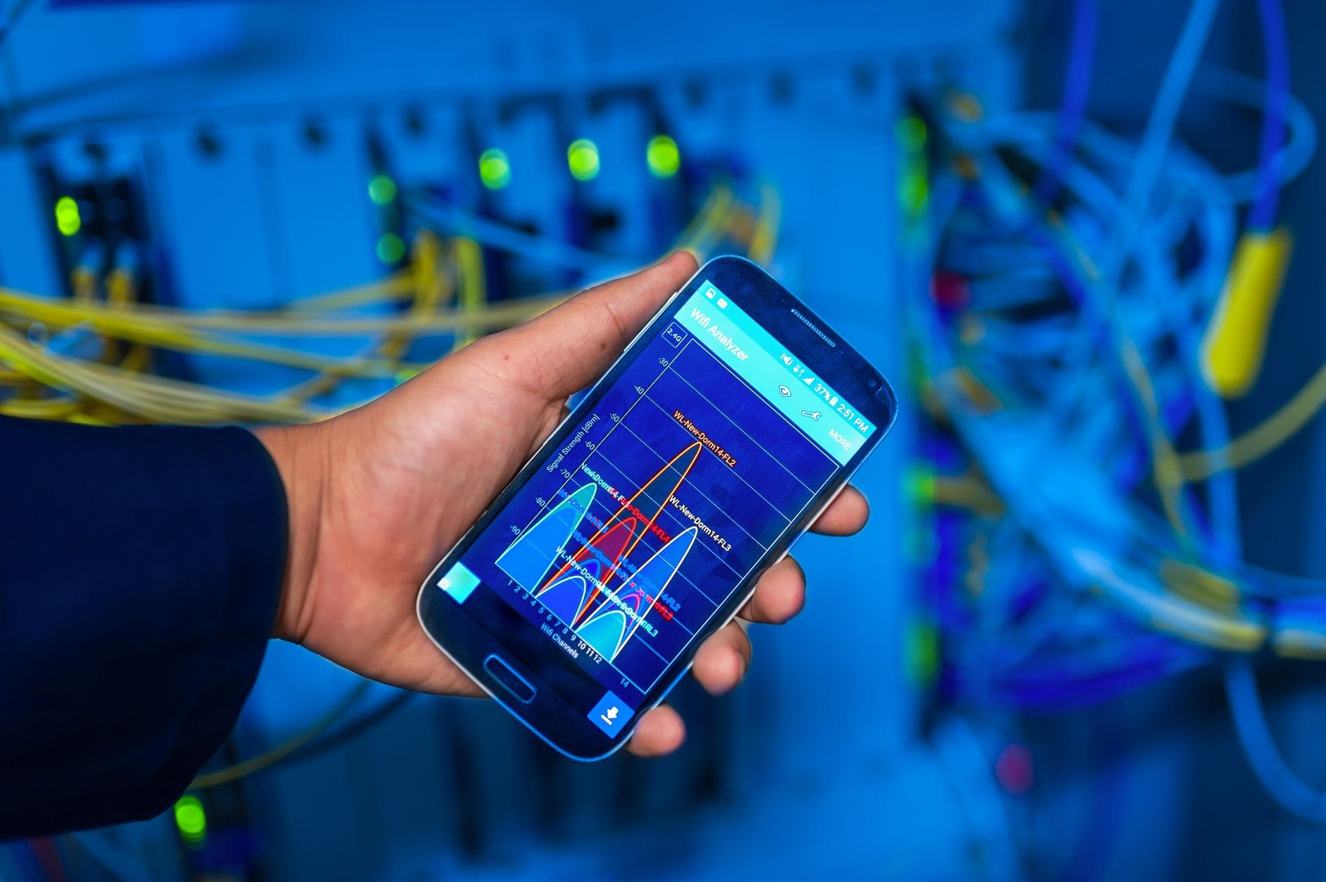 Dłoń trzyma smartfon z analizą sieci na tle serwerowni