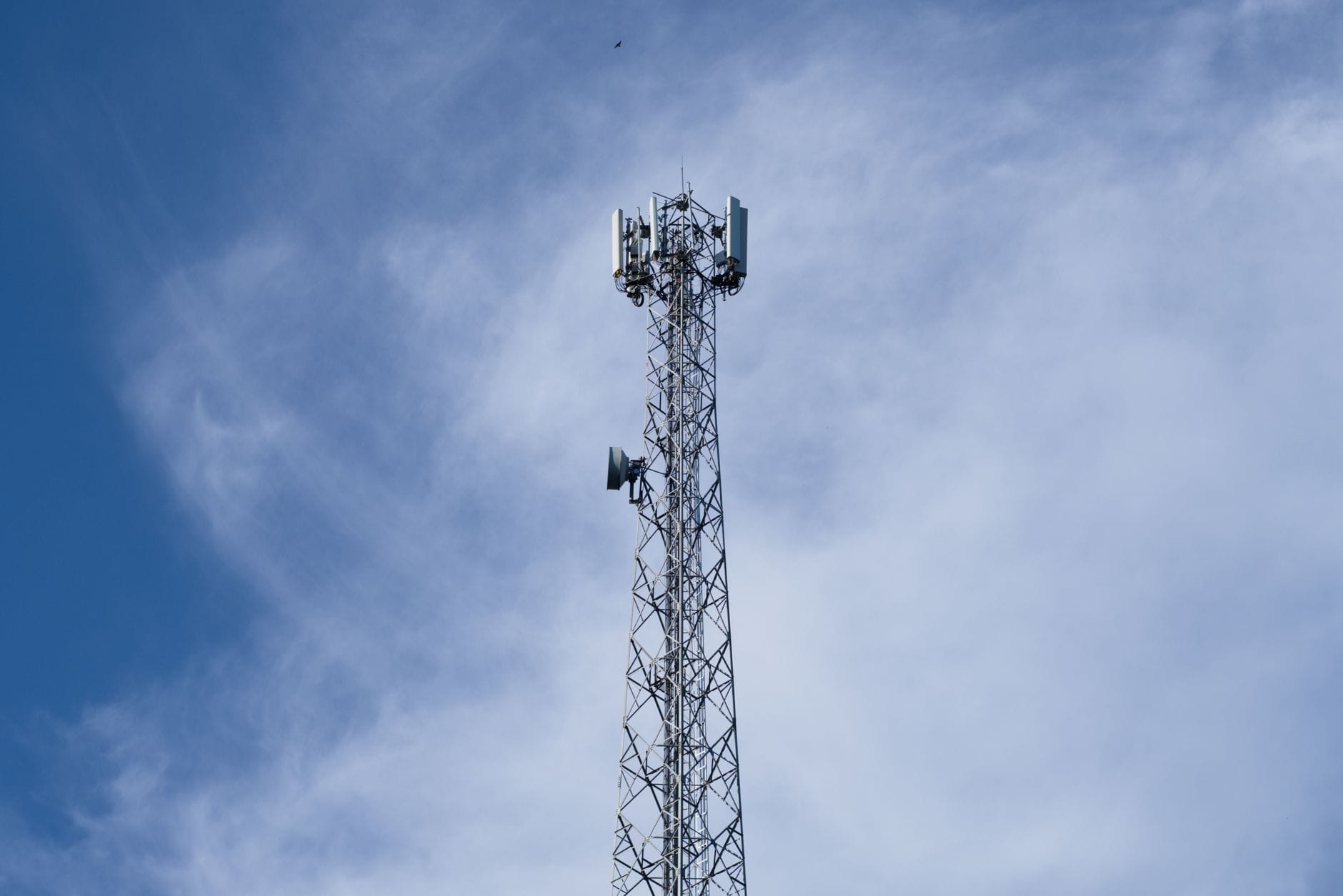 Metalowy maszt telekomunikacyjny na tle błękitnego nieba z chmurami
