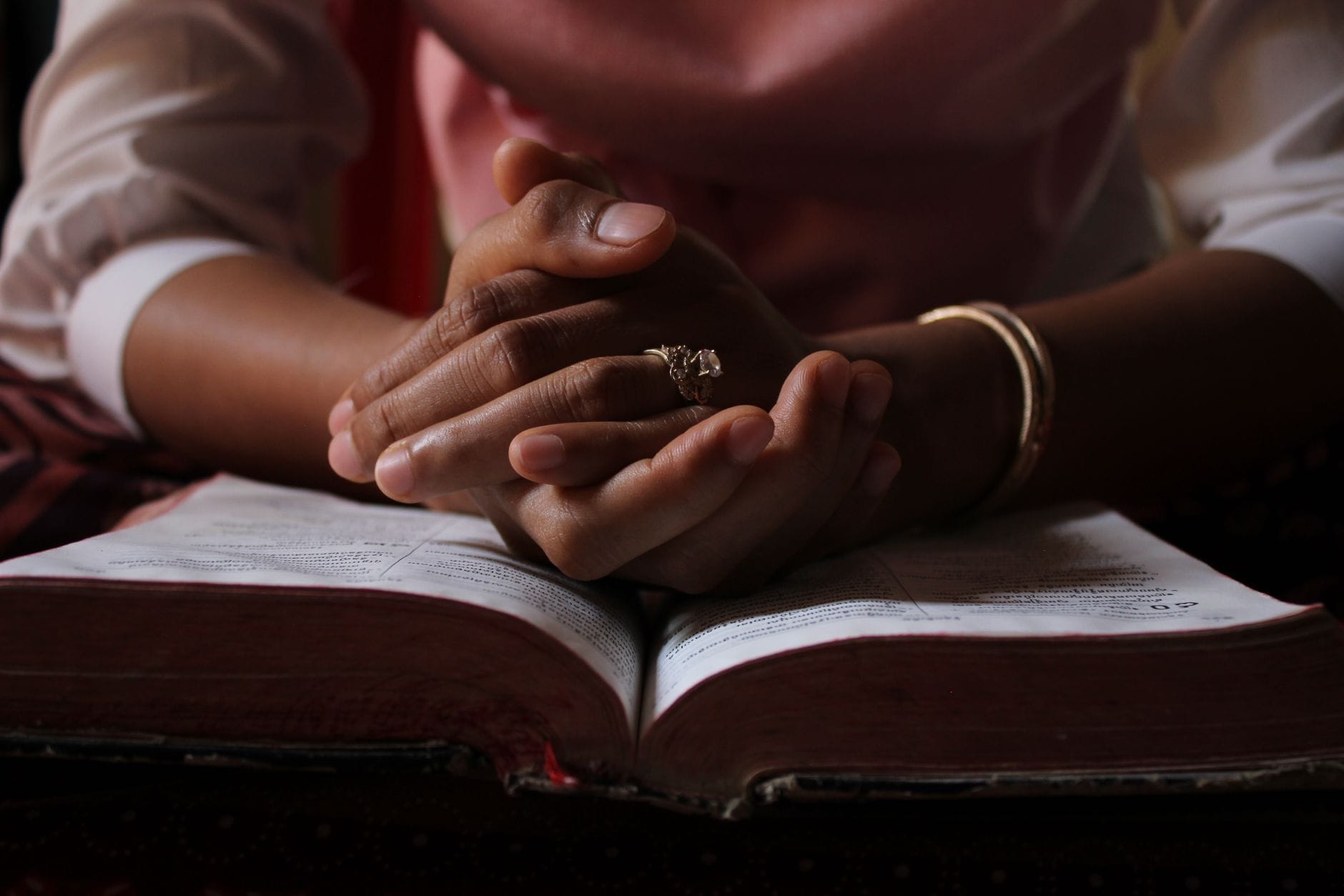 Złożone dłonie w modlitwie nad otwartą Biblią w skupieniu
