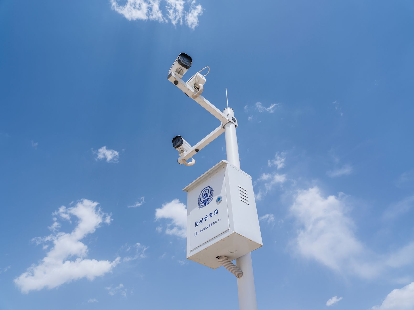 Białe kamery monitoringu na słupie na tle błękitnego nieba i chmur